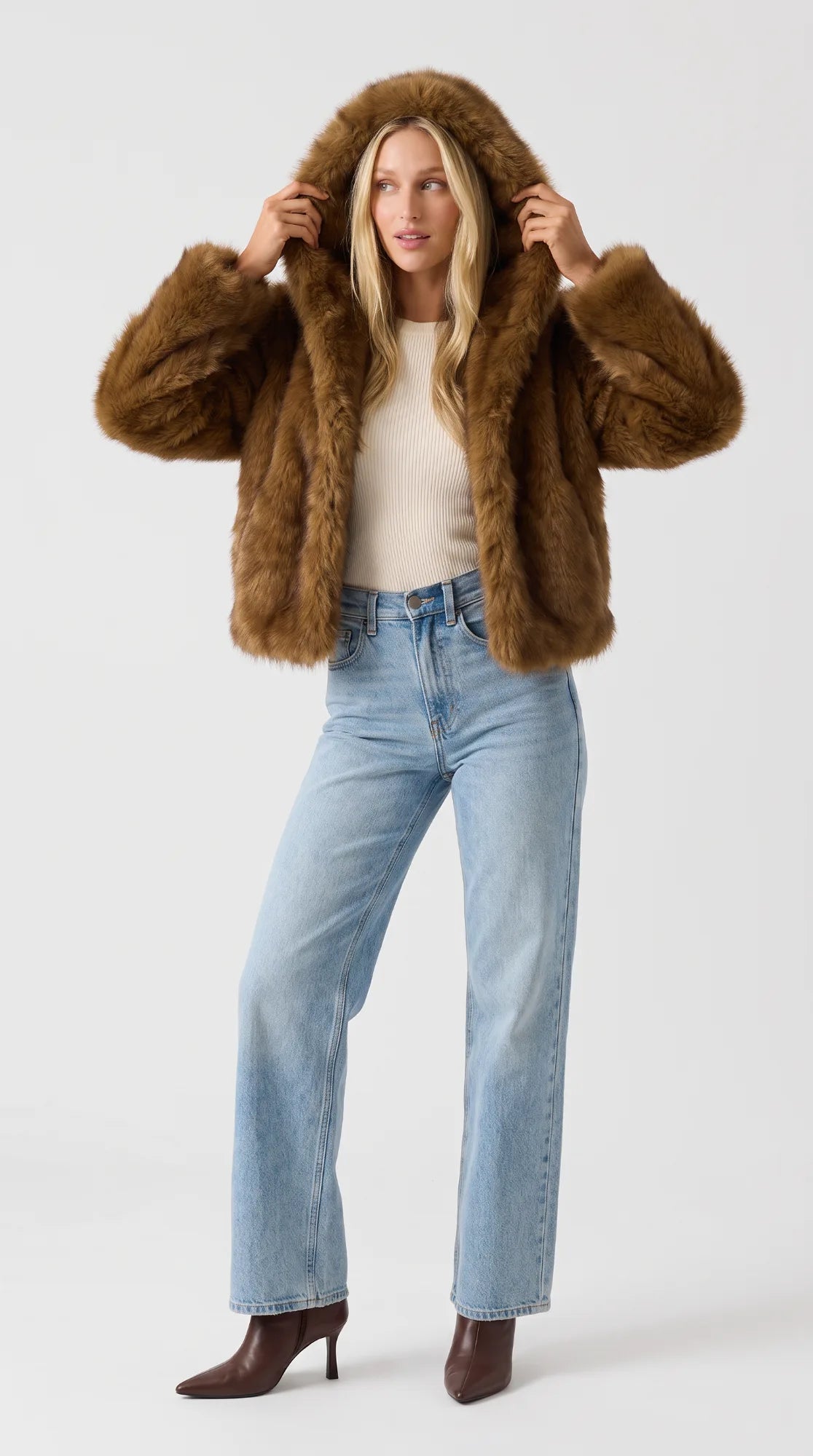 Brown faux fur jacket for women with the oversized hood worn up, framing her face, styled with light-wash jeans