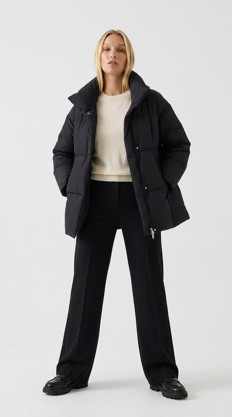 Black women's puffer jacket with stand collar worn open over a cream sweater and black trousers, front view